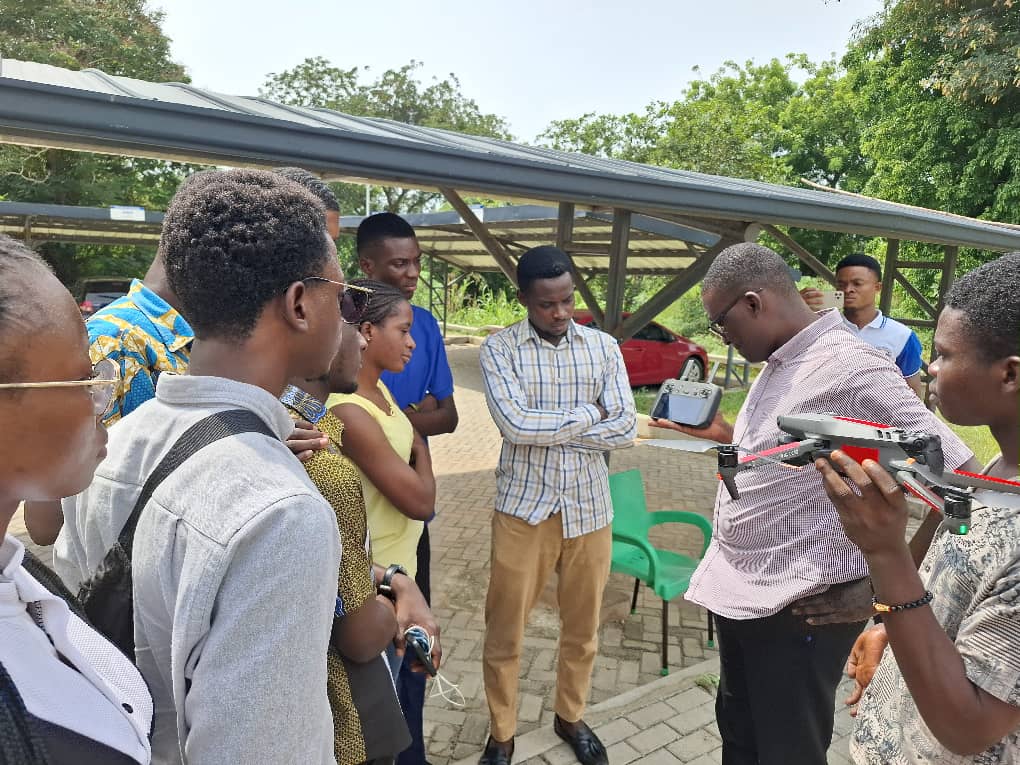 Drone instructor, Kwadwo, explaining the techniques for flying drones to graduate students, standing outside of the building 