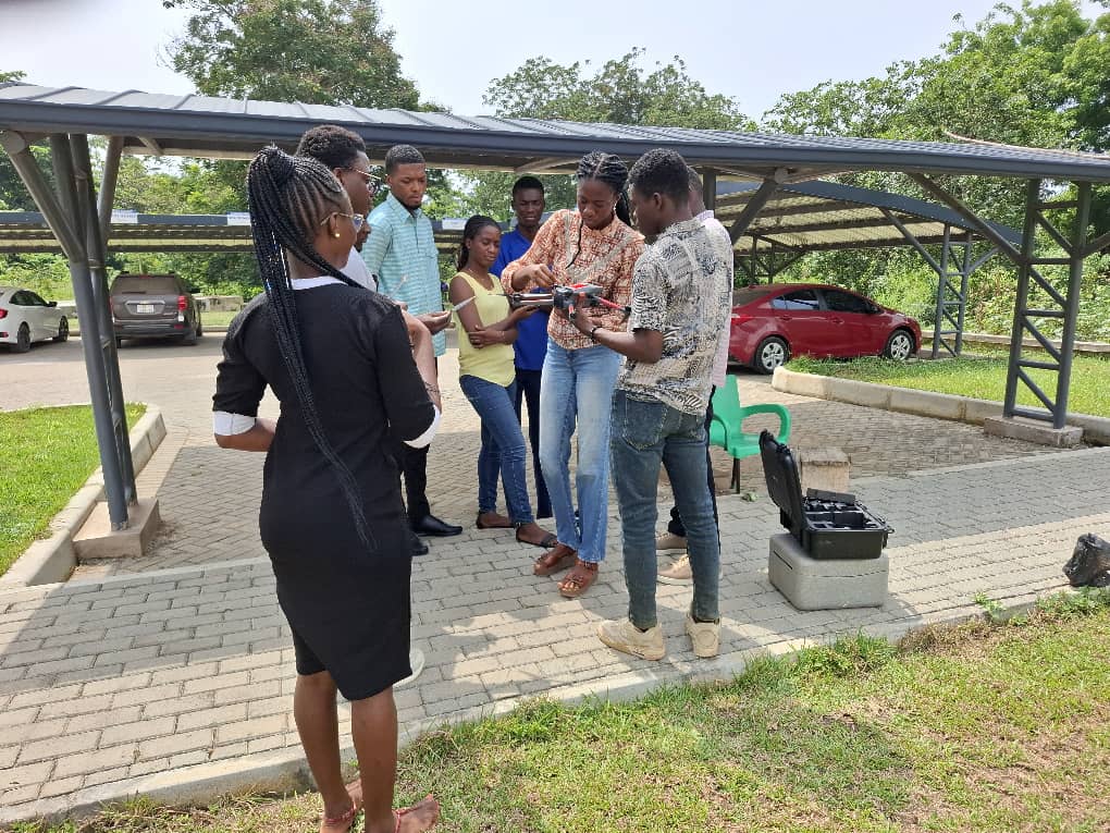 Drone instructor, Kwadwo, explaining the techniques for flying drones to graduate students, standing outside of the building 